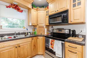 Kitchen featuring glass insert cabinets, stainless steel range with electric stovetop, black microwave, dark countertops, and light brown cabinetry