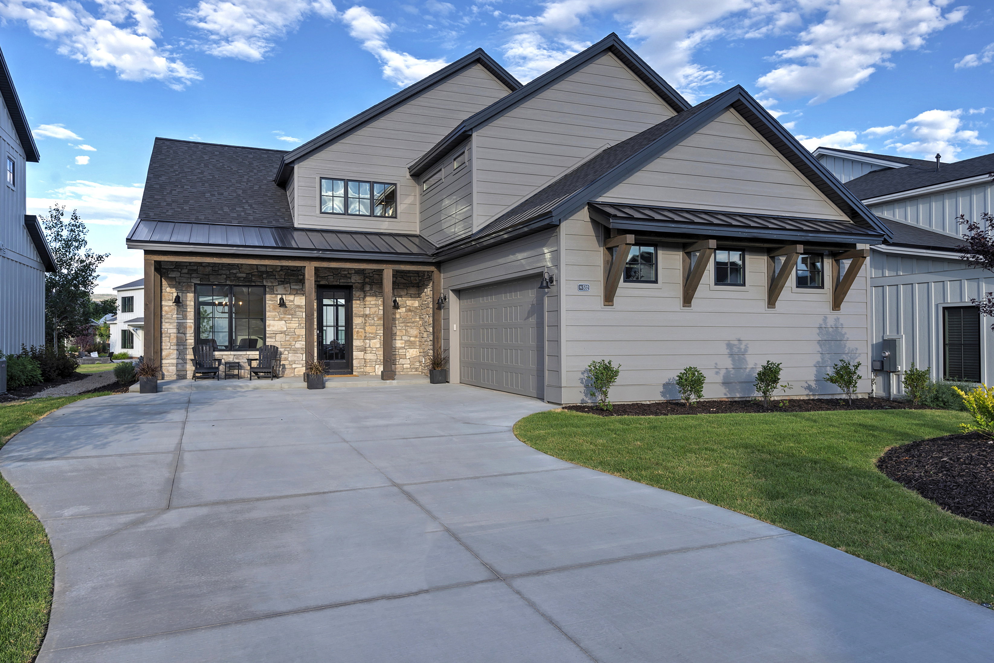 Modern farmhouse style home featuring driveway, a front lawn, an attached garage, and stone siding