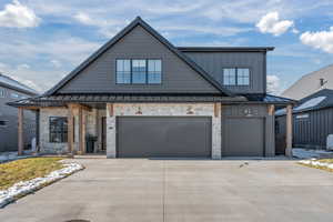 Modern inspired farmhouse with stone siding, a garage, concrete driveway, a standing seam roof, and a metal roof