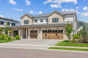 View of front of property featuring a standing seam roof, stone siding, a metal roof, and a garage