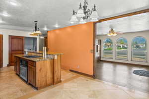Kitchen with dark stone counters, pendant lighting, a chandelier, a textured ceiling, and brown cabinetry