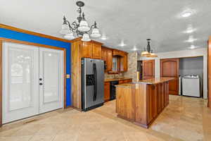 Kitchen with light stone counters, hanging light fixtures, brown cabinets, refrigerator with ice dispenser, and a chandelier