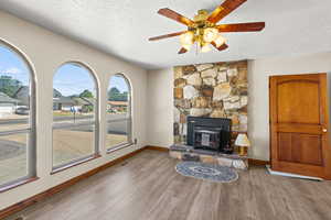 Living area featuring a textured ceiling, wood finished floors, a stone fireplace, and a ceiling fan