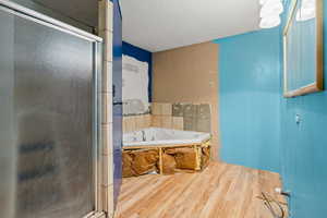 Bathroom with a shower stall, wood finished floors, a textured ceiling, and a garden tub