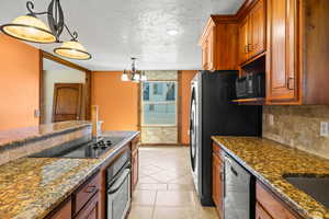 Kitchen featuring a textured ceiling, brown cabinetry, dark stone countertops, black appliances, and hanging light fixtures