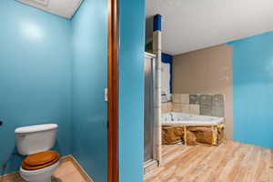 Bathroom featuring a garden tub, a textured ceiling, a shower stall, and light wood finished floors