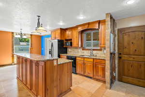 Kitchen featuring light stone counters, brown cabinetry, tasteful backsplash, a textured ceiling, and pendant lighting