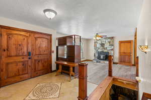 Foyer featuring ceiling fan, a textured ceiling, a stone fireplace, and light wood-style floors