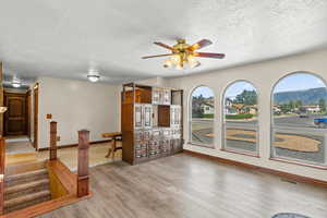 Unfurnished living room with ceiling fan, a textured ceiling, and light wood-type flooring
