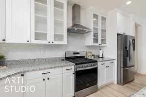 Kitchen featuring appliances with stainless steel finishes, wall chimney exhaust hood, light stone countertops, white cabinets, and recessed lighting