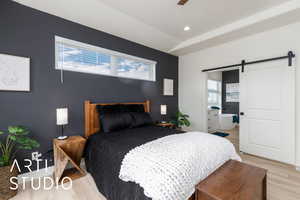 Primary Bedroom with a barn door, light wood finished floors, connected bathroom, recessed lighting, and a ceiling fan