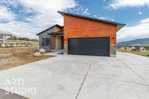 Modern home with stone siding, a mountain view, an attached garage, a standing seam roof, and concrete driveway