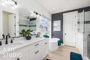 Primary Bathroom featuring a stall shower, a freestanding tub, double vanity, light wood-style flooring, and recessed lighting