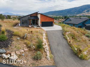 Contemporary house with a mountain view, stone siding, a standing seam roof, a garage, and asphalt driveway