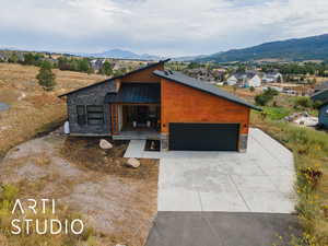 Modern home featuring stone siding, a standing seam roof, a metal roof, an attached garage, and concrete driveway