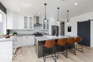 Kitchen with a barn door, glass insert cabinets, light stone countertops, white cabinetry, and an island with sink