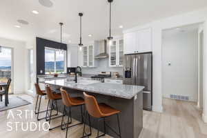 Kitchen featuring glass insert cabinets, appliances with stainless steel finishes, light stone counters, a kitchen bar, and white cabinets