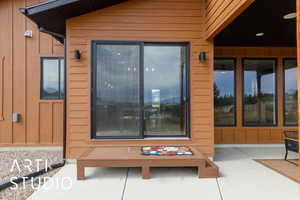 View of exterior entry with board and batten siding, a patio, and ceiling fan