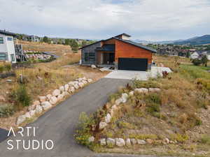 Contemporary home featuring stone siding, a garage, asphalt driveway, a metal roof, and a mountain view