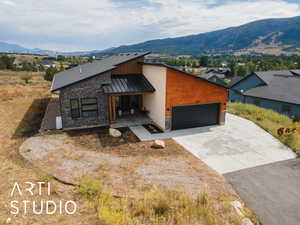 Contemporary home featuring a standing seam roof, an attached garage, stone siding, a metal roof, and a mountain view