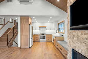 Kitchen with lofted ceiling, light wood-style floors, light brown cabinetry, recessed lighting, and white appliances