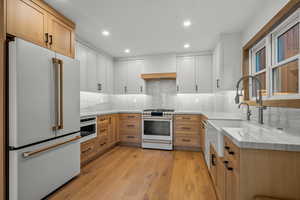 Kitchen with light stone counters, white appliances, recessed lighting, light brown cabinets, and light wood-style flooring