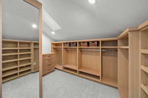 Spacious closet featuring vaulted ceiling, a skylight, and light colored carpet