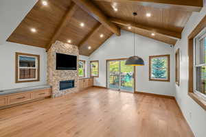 Unfurnished living room with light wood-type flooring, a fireplace, high vaulted ceiling, and a wood ceiling with exposed beams