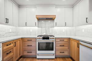 Kitchen with white appliances, light stone counters, custom range hood, tasteful backsplash, and recessed lighting