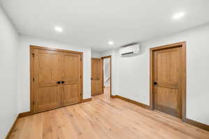 Unfurnished bedroom featuring light wood-style flooring, recessed lighting, a closet, and a wall mounted air conditioner