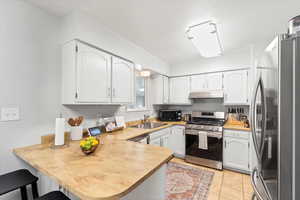 Kitchen featuring appliances with stainless steel finishes, a peninsula, white cabinetry, light tile patterned floors, and light countertops