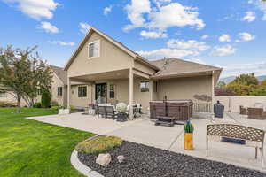 Back of house featuring a hot tub, a patio, stucco siding, and roof with shingles