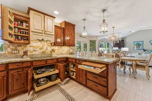 Kitchen with open shelves, decorative backsplash, a peninsula, hanging light fixtures, and light stone counters