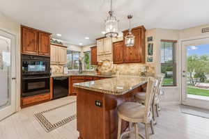 Kitchen featuring backsplash, a breakfast bar, a peninsula, black appliances, and hanging light fixtures