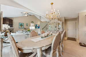 Dining room with stairs, a chandelier, light wood-style flooring, a stone fireplace, and lofted ceiling