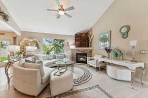 Living room featuring light wood-style floors, a stone fireplace, a ceiling fan, and vaulted ceiling