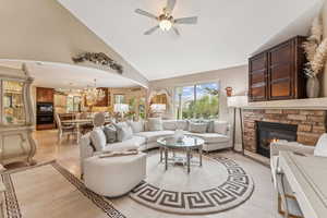 Living area featuring high vaulted ceiling, a stone fireplace, light wood finished floors, a chandelier, and arched walkways