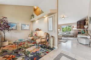 Sitting room featuring a fireplace, a ceiling fan, tile patterned floors, high vaulted ceiling, and inlaid floor details