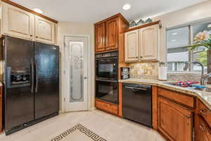 Kitchen with black appliances, decorative backsplash, recessed lighting, light stone countertops, and light wood-style floors