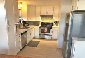 Kitchen featuring appliances with stainless steel finishes, white cabinetry, backsplash, light wood-type flooring, and light stone countertops