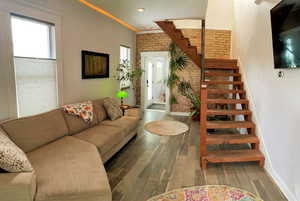 Living area with stairs, healthy amount of natural light, wood finished floors, brick wall, and crown molding