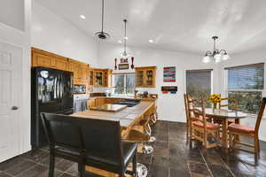 Kitchen featuring black fridge with ice dispenser, glass insert cabinets, vaulted ceiling, pendant lighting.