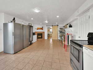 Kitchen with a barn door, appliances with stainless steel finishes, light tile patterned floors, a textured ceiling, and a warm lit fireplace