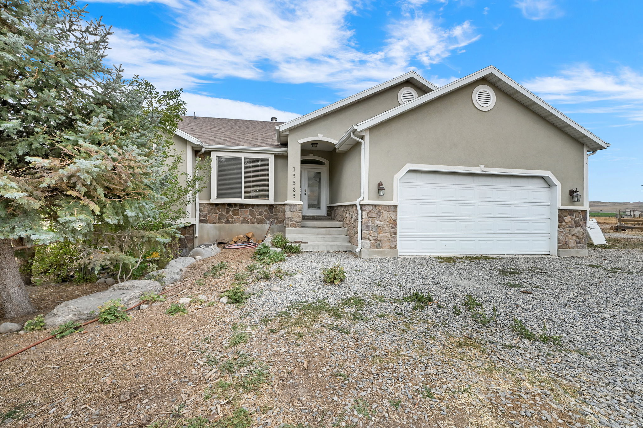 Ranch-style house with a garage, driveway, stone siding, and stucco siding