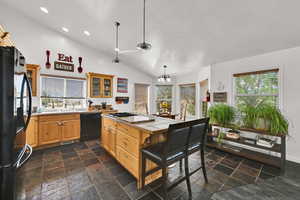 Kitchen featuring black appliances, lofted ceiling, tile counters, pendant lighting, and glass insert cabinets