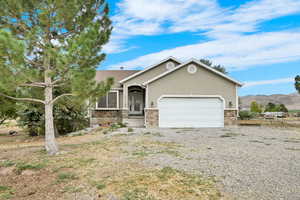 Ranch-style house with an attached garage, gravel driveway, stone siding, and stucco siding