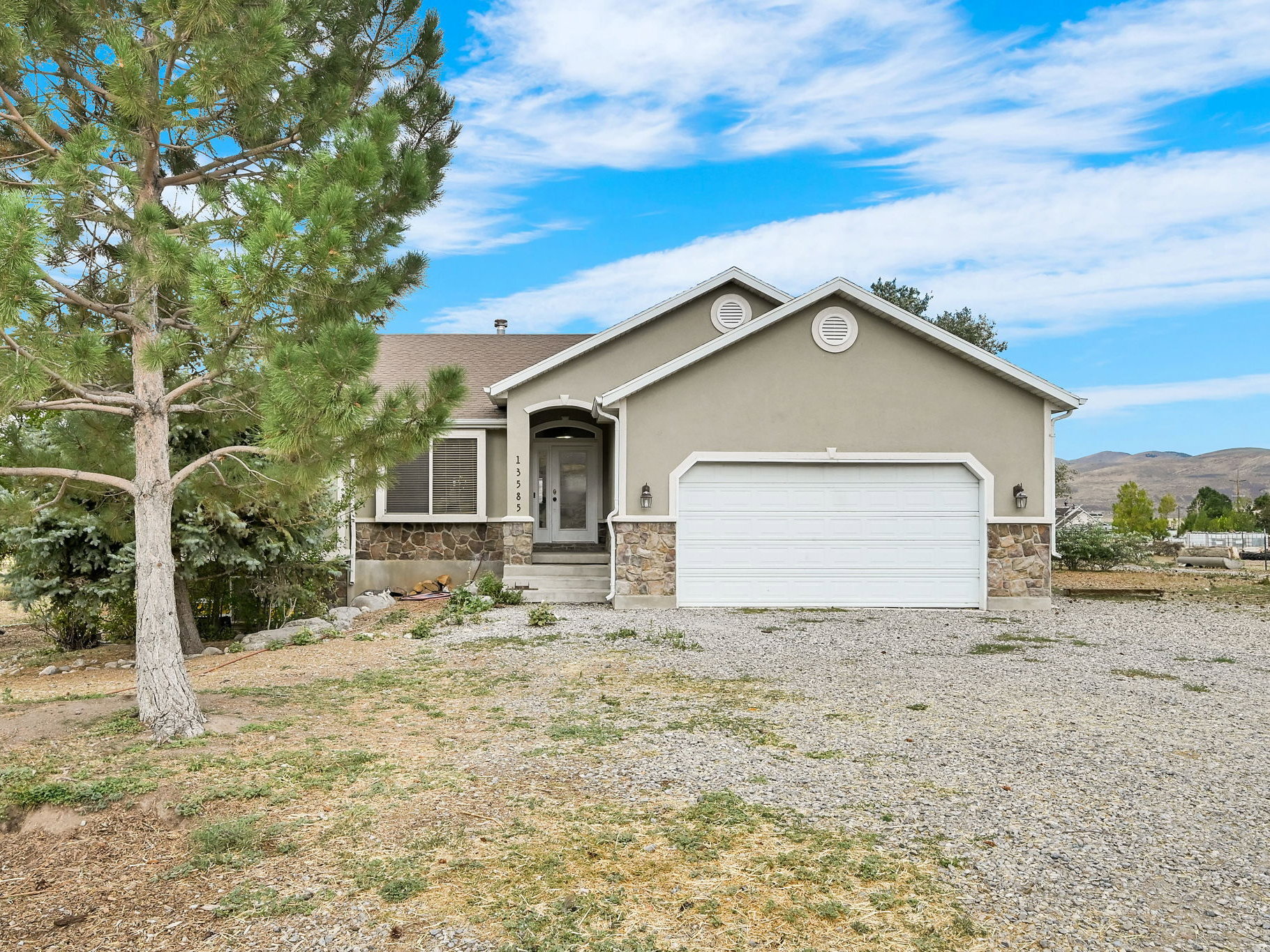Ranch-style house with an attached garage, gravel driveway, stone siding, and stucco siding