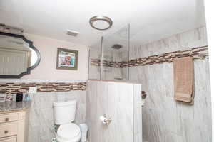 Full bath with vanity, walk in shower, tile walls, and a textured ceiling