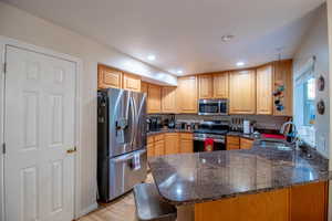 Kitchen with a peninsula, appliances with stainless steel finishes, dark stone countertops, light wood-style flooring, and recessed lighting