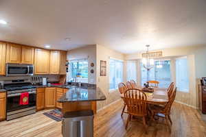Kitchen with appliances with stainless steel finishes, light wood-type flooring, dark stone counters, recessed lighting, and a textured ceiling